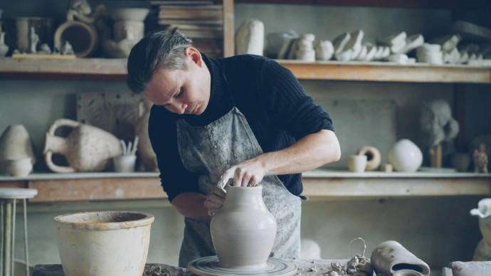 A potter is shaping a clay vase on a wheel.